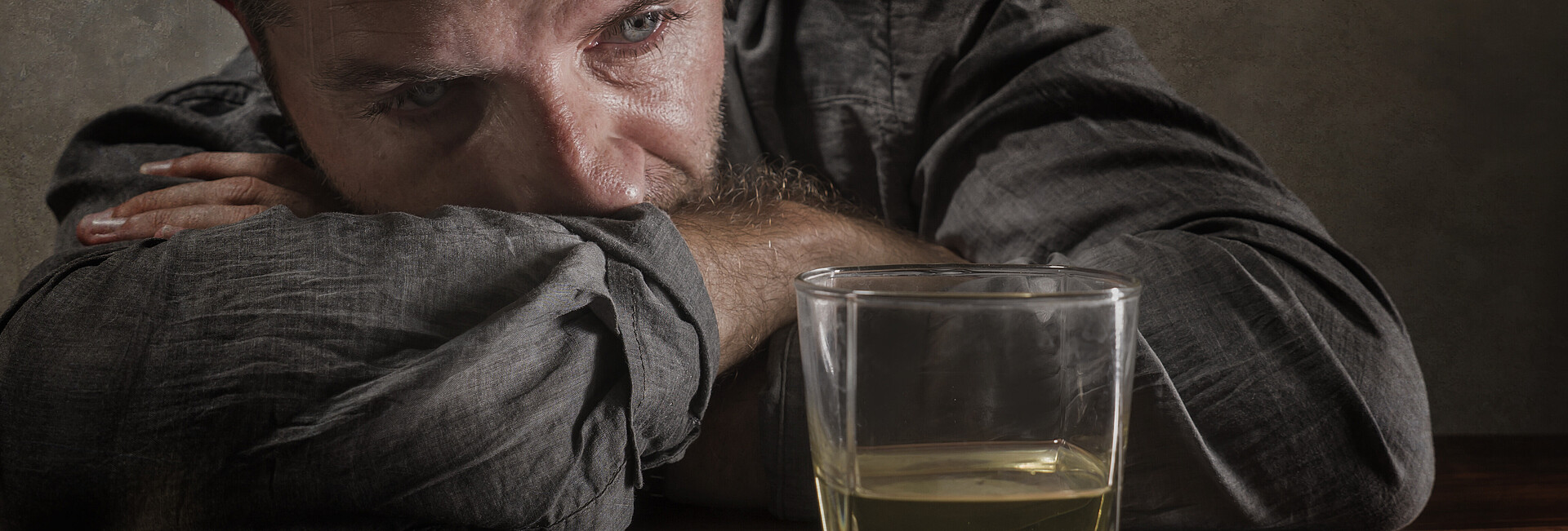 Mann sitzt traurig vor einem Glas mit Alkohl