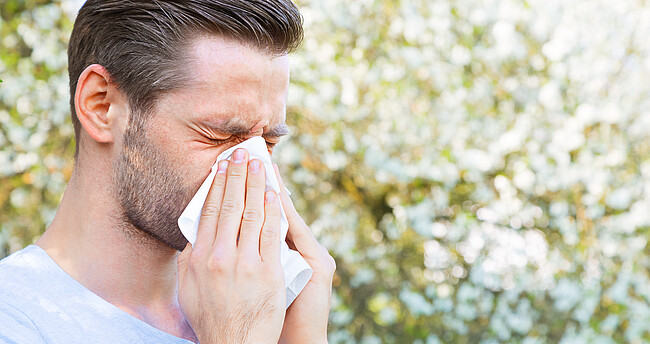 Mann schnäuzt in Taschentuch aufgrund Pollenallergie im Frühling