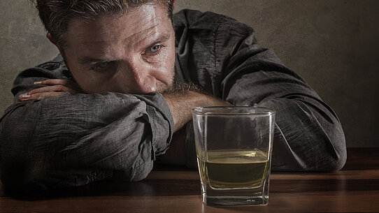 Mann sitzt traurig vor einem Glas mit Alkohl