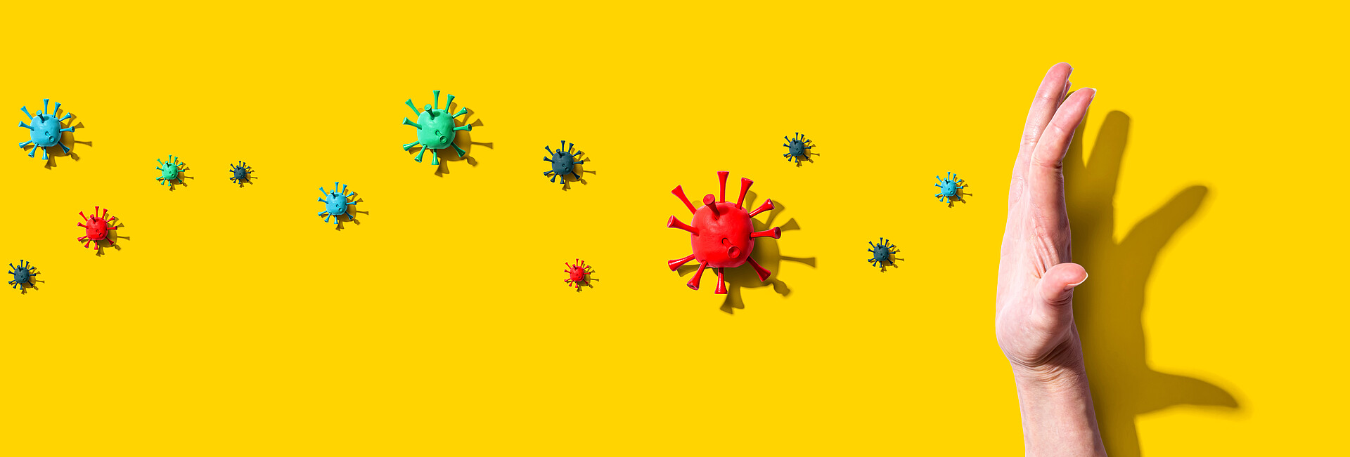 Hand vor gelbem Hintergrund hält verschiedene Viren auf