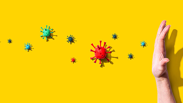 Hand vor gelbem Hintergrund hält verschiedene Viren auf