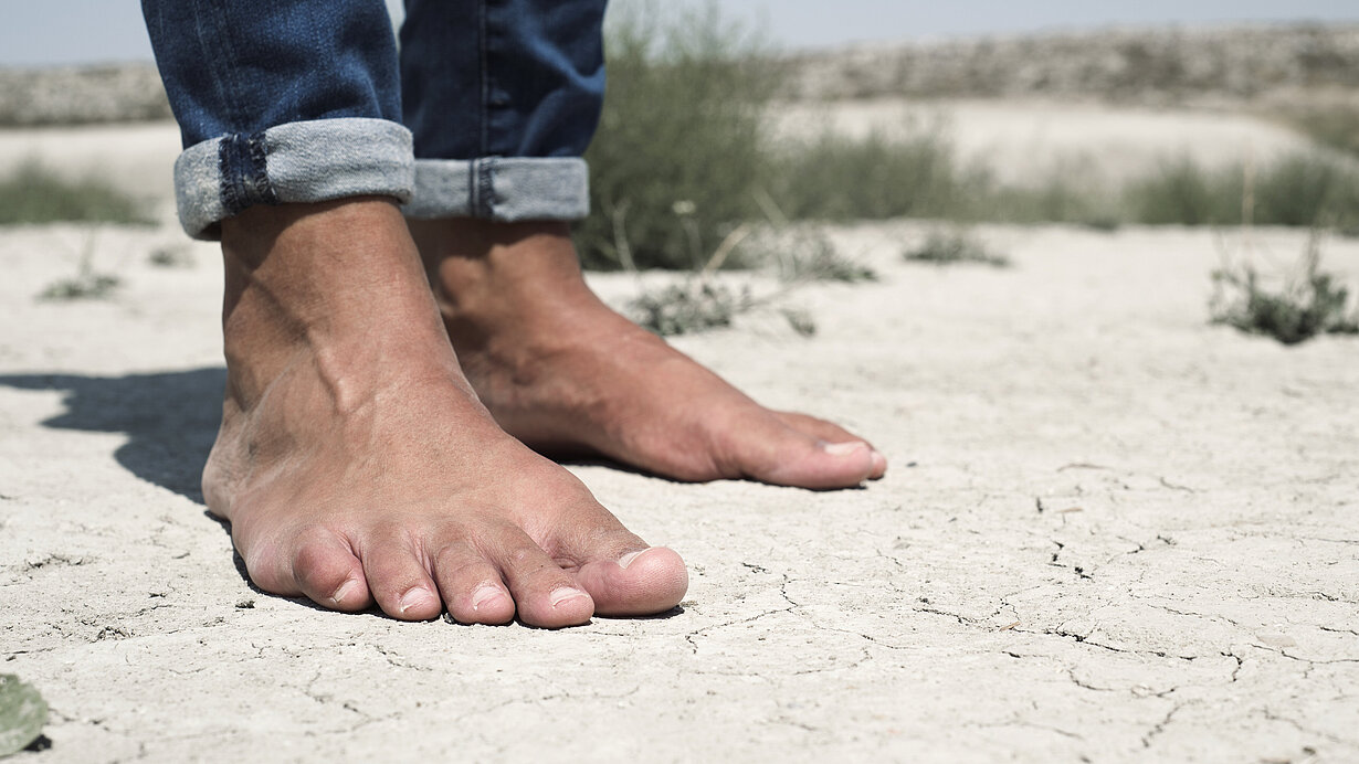 Nackte Männerfüße auf einem rissigen, trockenen Boden