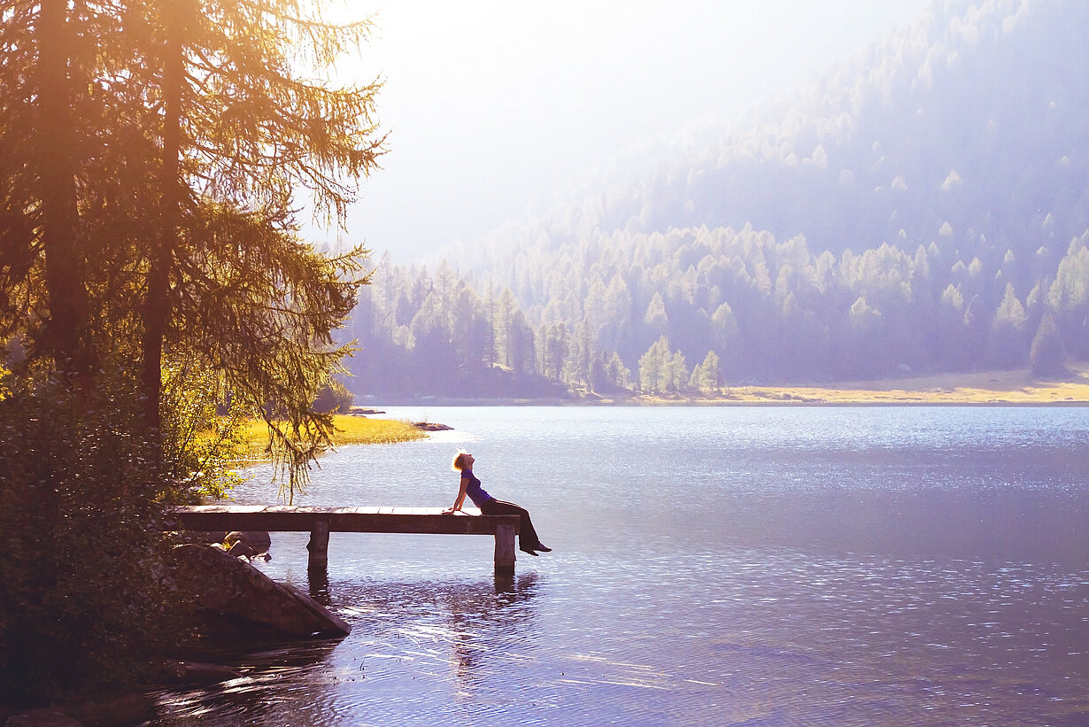 Eine Frau sitzt bei Sonnenschein am Ende eines Steges an einem See
