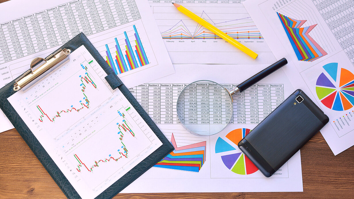 Diagramme, Bleistift, Lupe und ein Mobiltelefon liegen auf einem Tisch