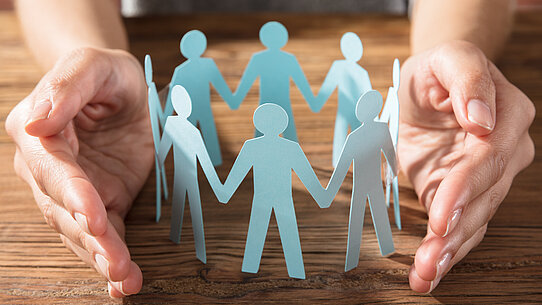 Hände schützen ausgeschnittene Papierfiguren