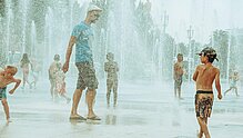Kinder und Erwachsene plantschen in einem Brunnen in der Stadt