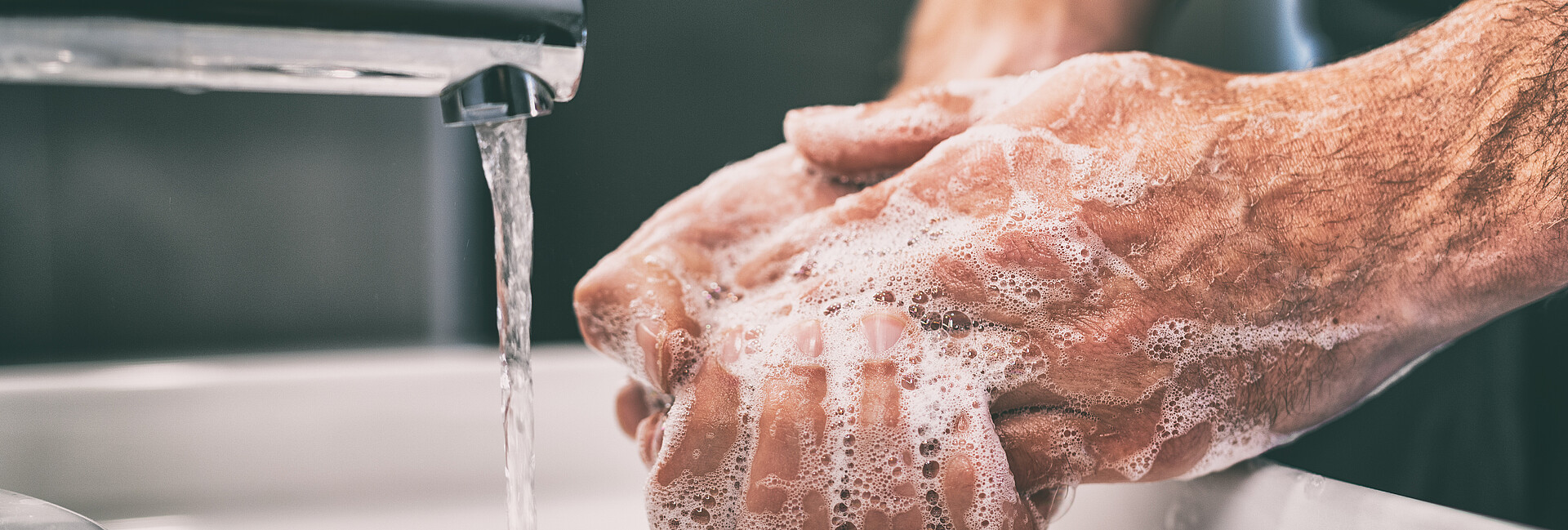 Mann wäscht sich die Hände am Waschbecken unter fließendem Wasser