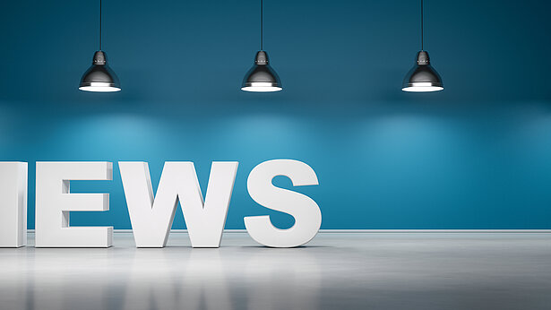 Schriftzug "News" vor blaugrüner Wand mit 5 Lampen