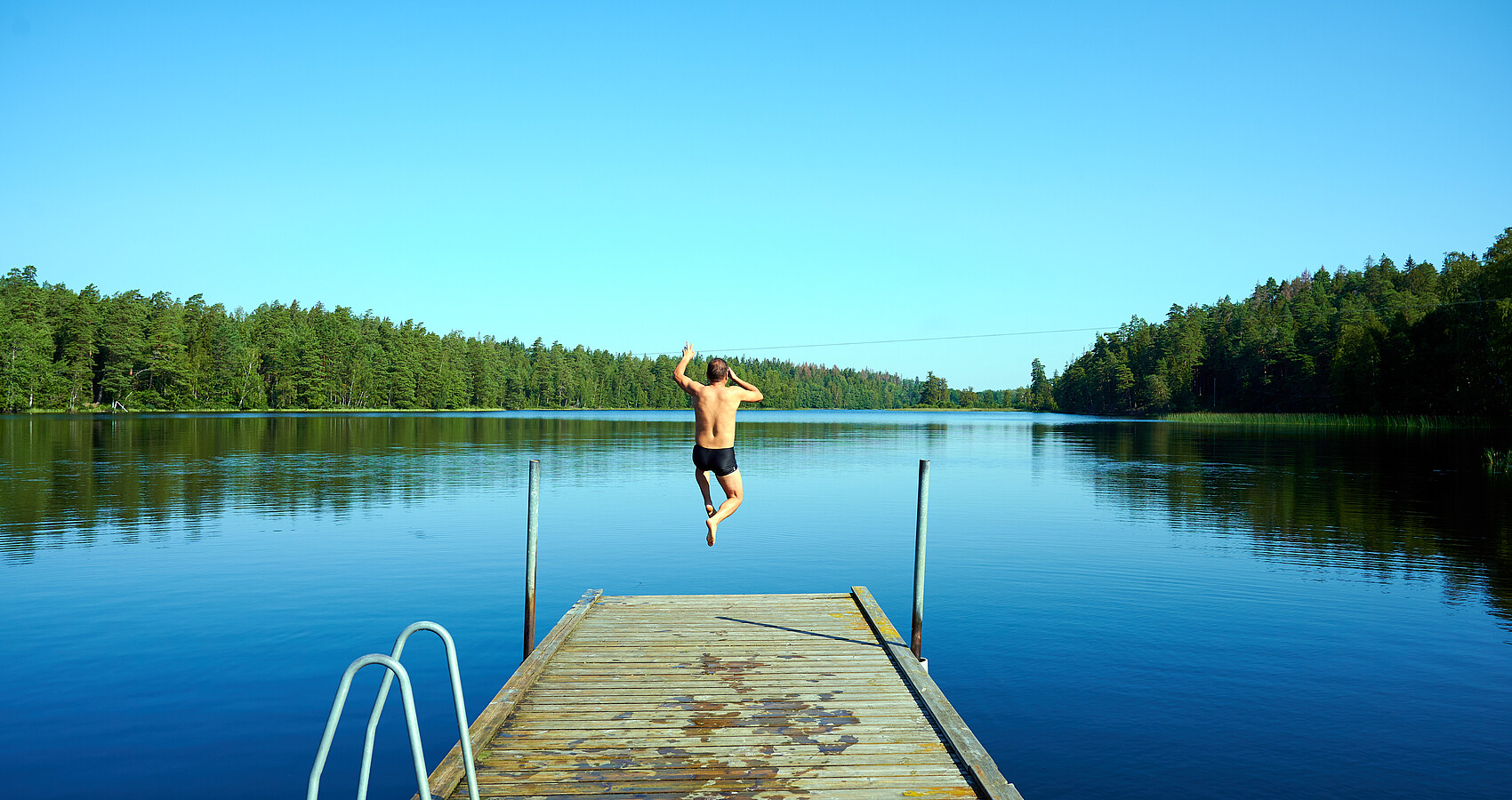 Mann springt vom Holzsteg in einen See
