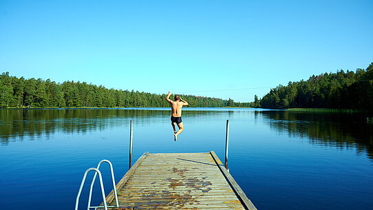 Mann springt vom Holzsteg in einen See