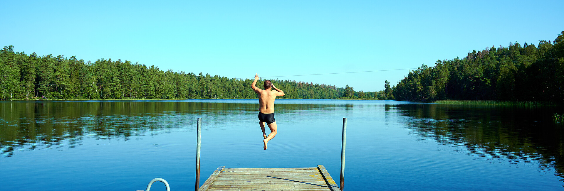 Mann springt vom Holzsteg in einen See