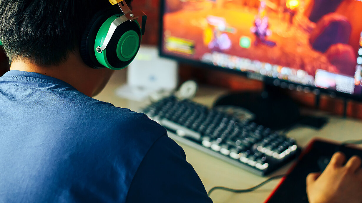 Junger Mann spielt mit Kopfhörern Spiele am Computer