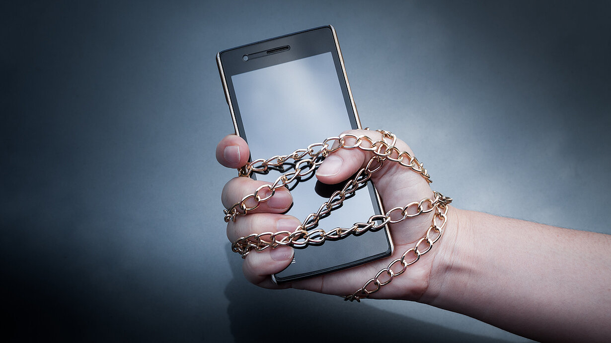 Eine Hand mit einer Kette an ein Smartphone gekettet