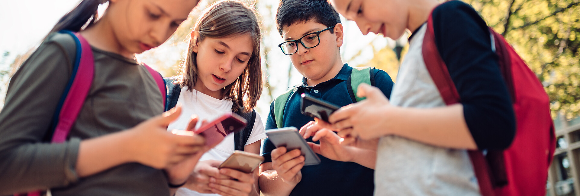Schulkinder stehen zusammen und benutzen Handys