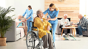 Eine Pflegerin gibt einer Seniorin im Rollstuhl ein Glas Wasser