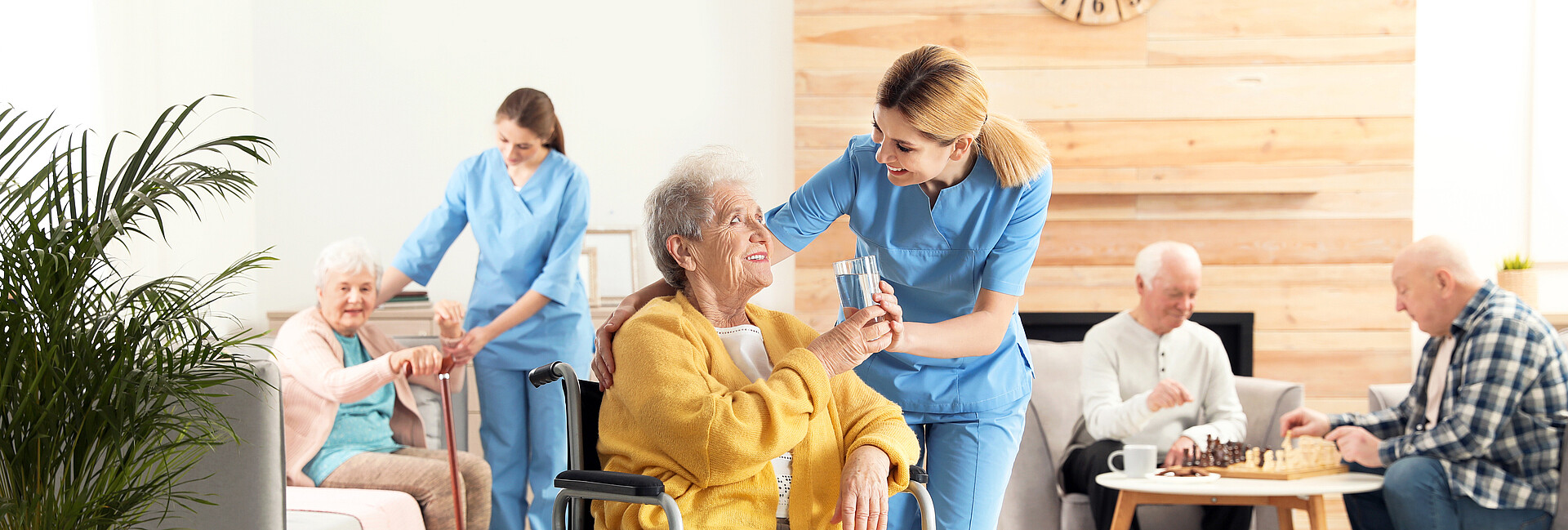 Eine Pflegerin gibt einer Seniorin im Rollstuhl ein Glas Wasser