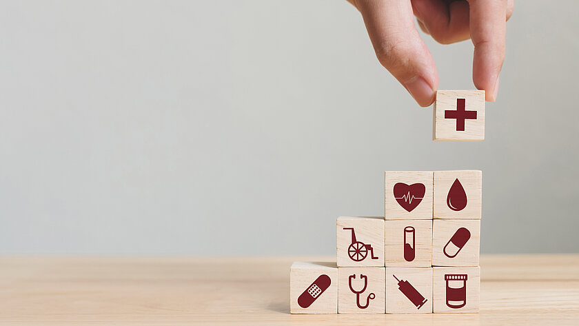 Hand stapelt kleine Holzwürfel auf denen Gesundheitssymbole abgebildet sind