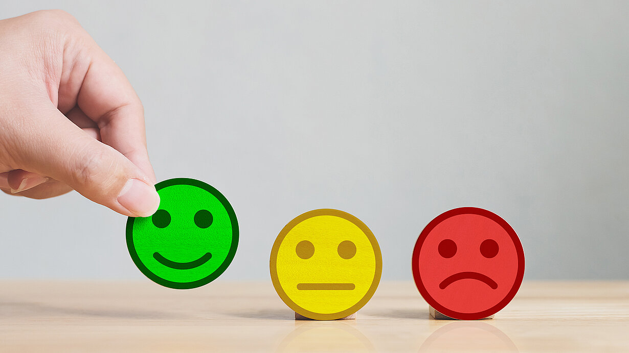 Hand wählt grünes Holzplättchen mit Smileysymbol