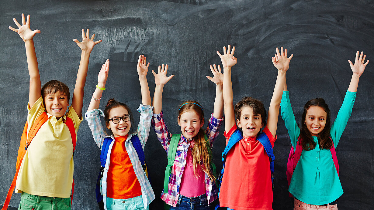 Fünf fröhliche Schulkinder vor einer Schultafel