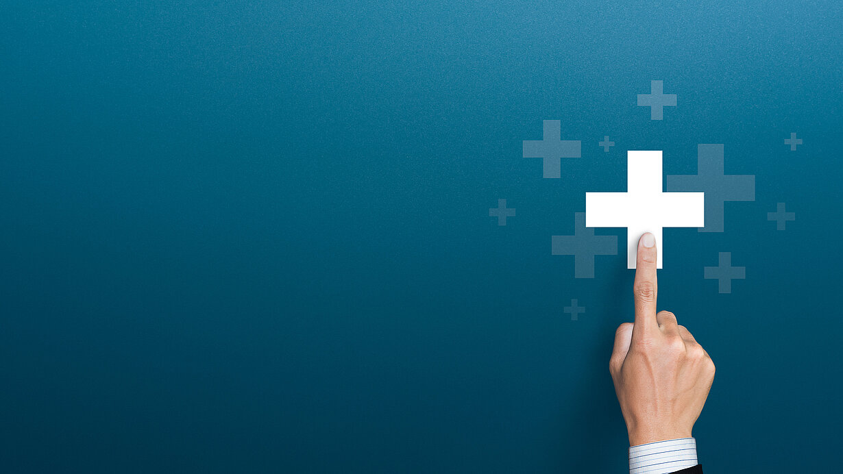 Hand zeigt auf weißes Pluszeichen vor blauem Hintergrund